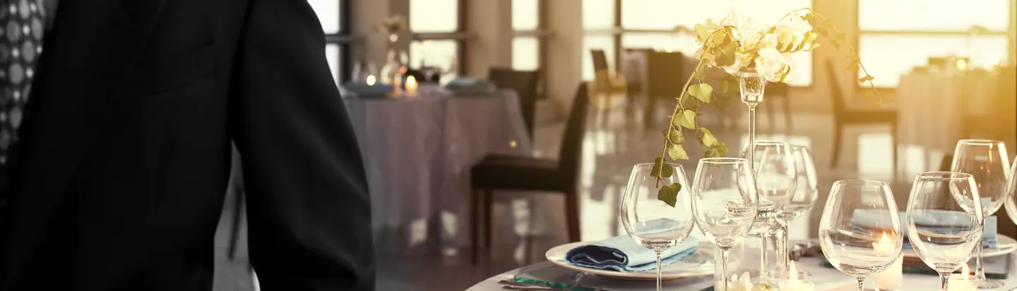 Bilde av en person i dress med flere bord i en resturant bak