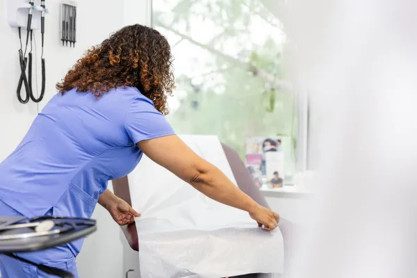 Sykepleier/Lege som legger papirduk på en undersøkelsesbenk