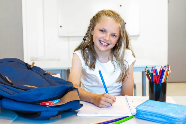 Barn som ser mot kamera mens det holder en blyant i hånden og skriver