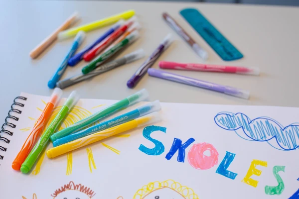 Ett bord med masse tusjer og ett tegneark med tegning på