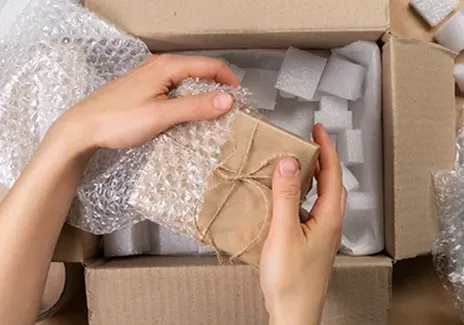 En person som pakker in en brun pakke med bobbleplast over en eske med støttdemping fyll inni