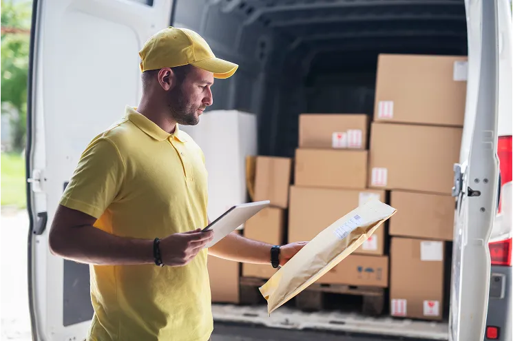 En person som leser på en pakke foran en varebil full av pakker