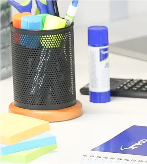 Ett skrivebord med notatbok, lim, pen, tusj, saks og post-it lapper