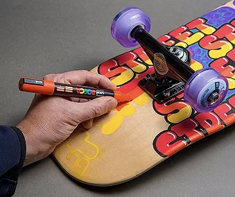 En person som tegner på ett skateboard med posca tusj