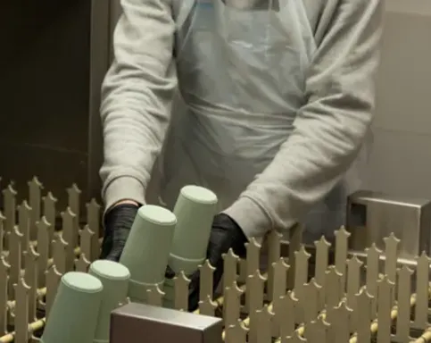 En person som vasker return & reuse kopper i en industrivaskemaskin