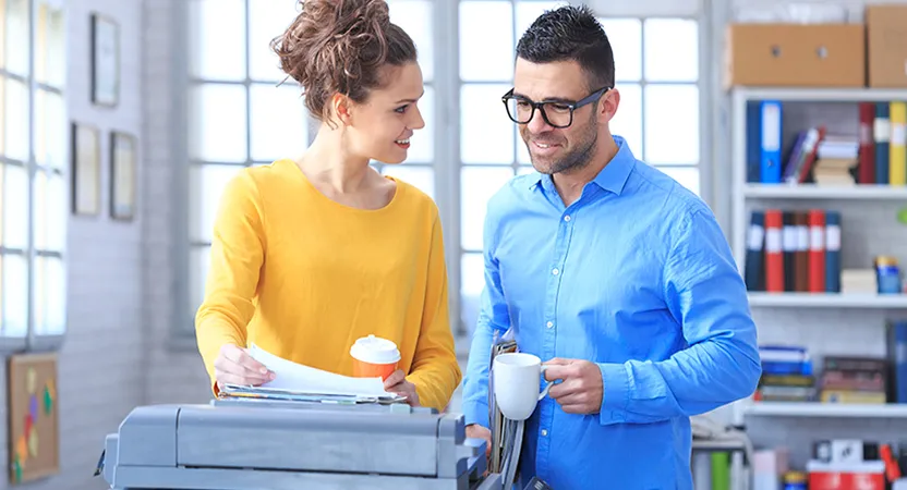 2 personer som står med en kaffekopp i hånden ved en skrive/kopimaskin