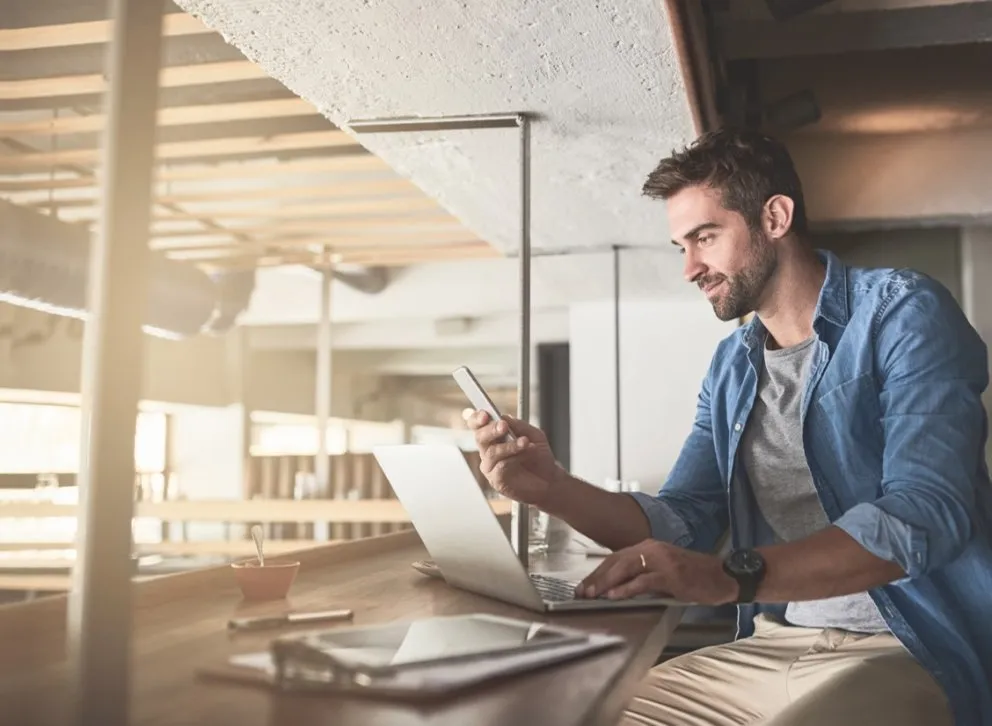 Person jobber på laptop og mobil i moderne kontorlokale