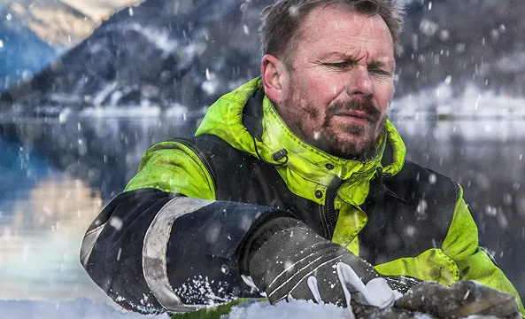 En person med hansker og en arbeidsjakke som jobber mens det snør