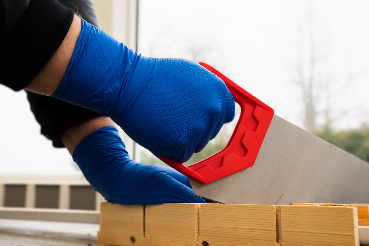 En person med engangshansker som sager treverk