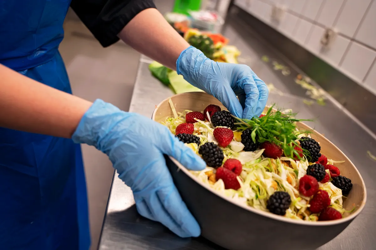 En person med engangshansker som tilbreder mat