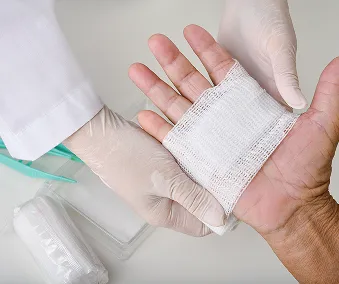 En person som har på seg engangshansker, mens de bandasjerer en annen person