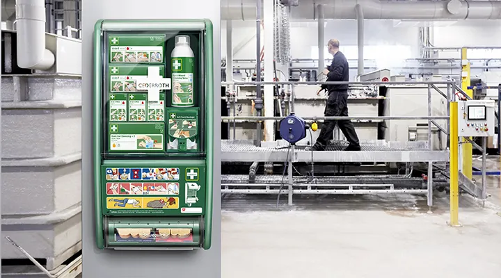 En førshjelpstasjon hengende på en søyle i front, mens en person jobber i ett industri område i backgrunnen