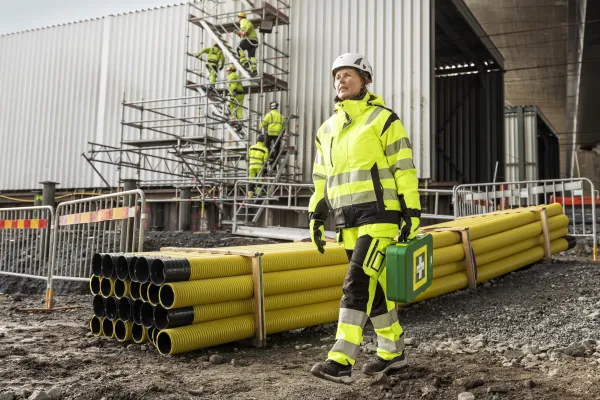 En person på en arbeidsplass i verneutstyr som bærer på en førstehjelpskoffert
