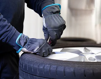 En person med arbeidshansker som jobber på et bilverksted. Setter nytt dekk på en bilfelg