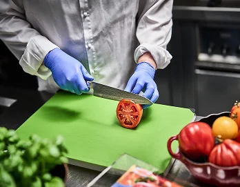 En person med blå engangshansker som holder en kniv og kutter en tomat på ett skjærebrett