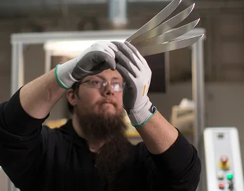 En person med arbeidshansker som holder opp noen metall biter og ser på de