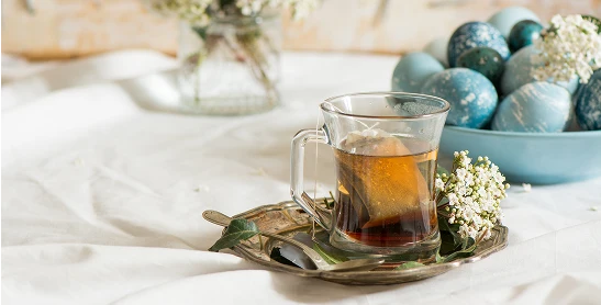 En kopp med te på ett bord med en duk og en bolle med diverse egg farget i varierende gråblå farger