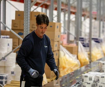 En person på lager som jobber ved ett pakkebånd