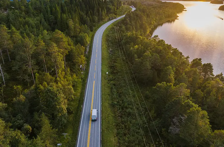En bil som kjører på en vei omringet av skog, vann og natur