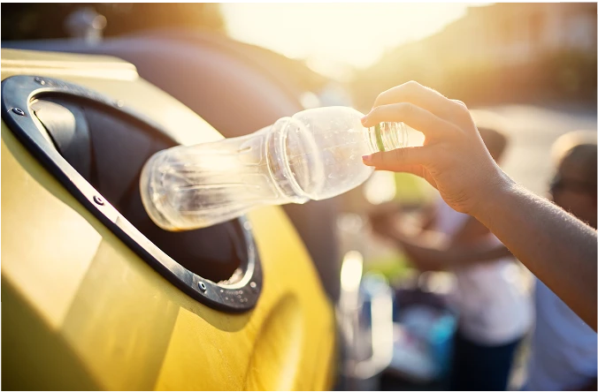 En person som kaster en plastflaske i en kildesorteringsbeholder