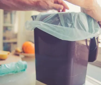 En person som setter en matavfallspose i en avfallsbeholder for kildesortering