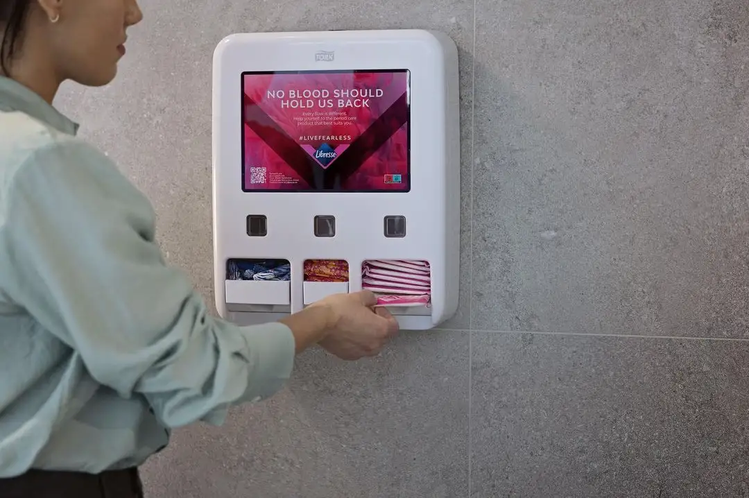 En person som bruker en dispenser for mensenprodukter på et toalett