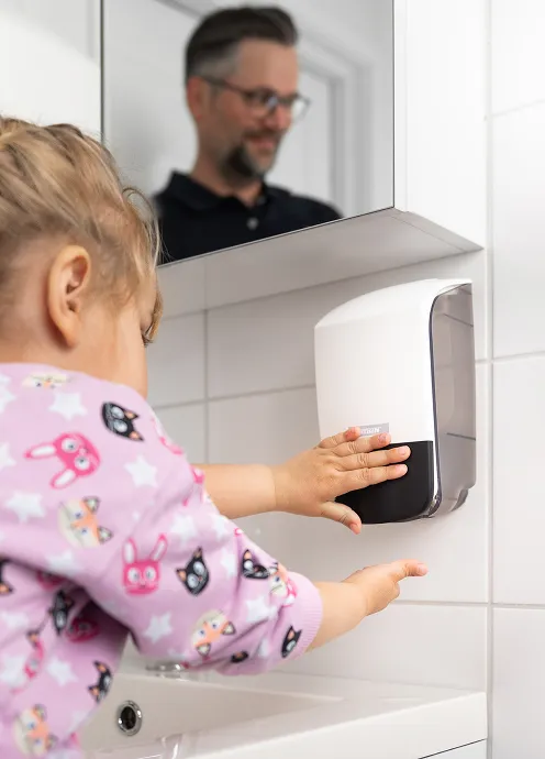 Barn bruker en Katrin såpedispenser ved vask, med voksen i bakgrunnen.