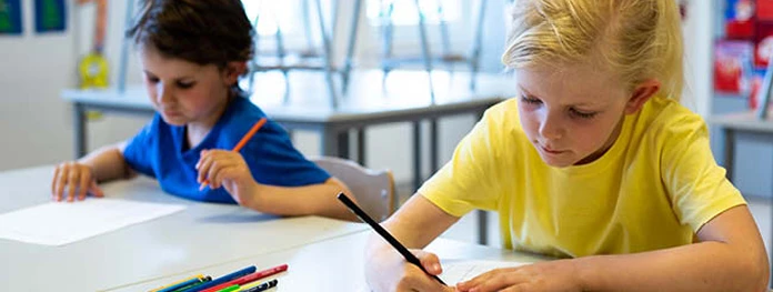 2 skolebarn som sitter ved en pult og skriver på ett ark
