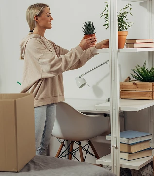 En person som rydder ut av en pappeske og setter blomster på hylle