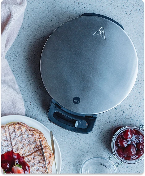 Ovenfra bilde av ett vaffeljern med vaffel og syltetøy på siden