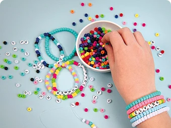 En person som tar perler ut av en boks, med armbånd og perler løst på bordet