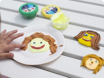 En person som lager ansikter med Playbox leire på en papp tallerken