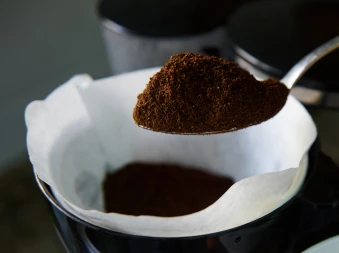 Bilde av en skje med ferdigkvernet kaffe som er over ett kaffefilter