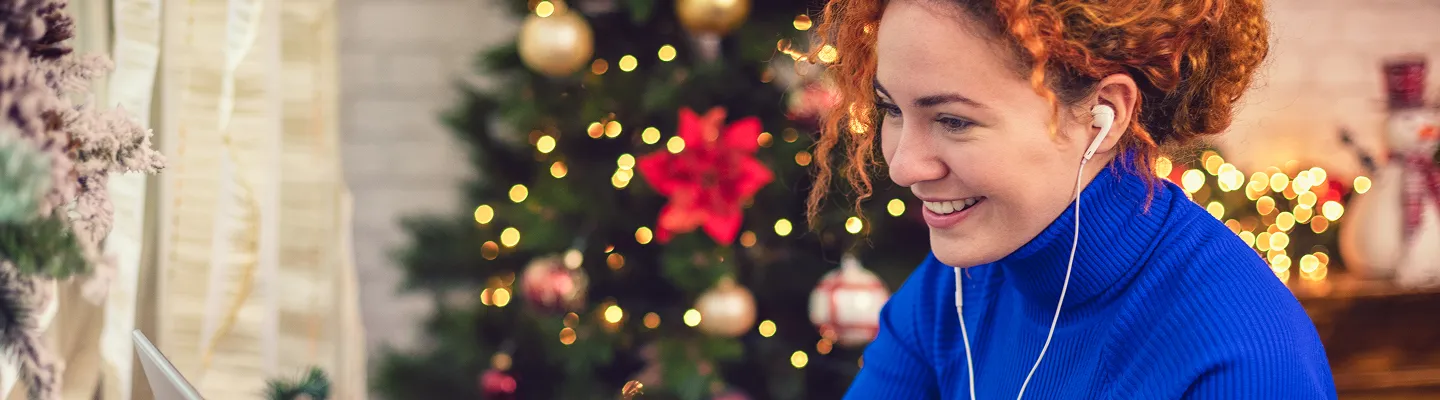 En person i blå genser som smiler, med ett juletre i bakgrunnen