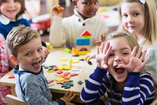 Barn som ser mot kamera mens siter ved ett bord me diverse leker og spill