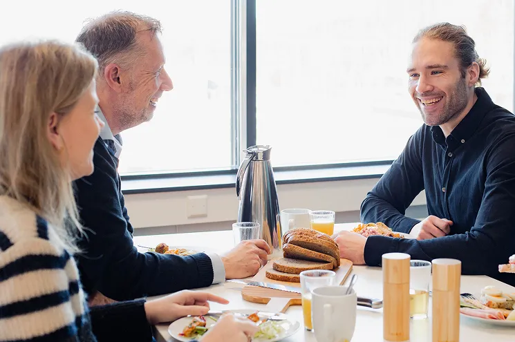 Tre person som sitter og prater mens de har lunsj